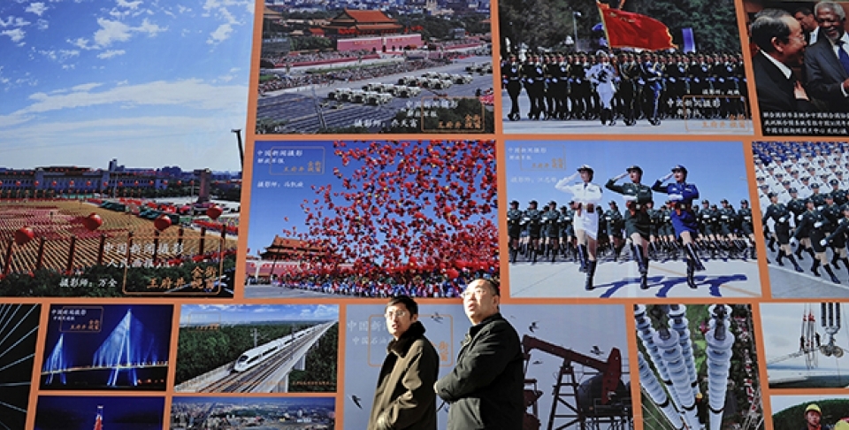 Two Chinese men walk past a huge billboard featuring photos of China's development in previous years in Beijing. (AP Photo/Andy Wong)