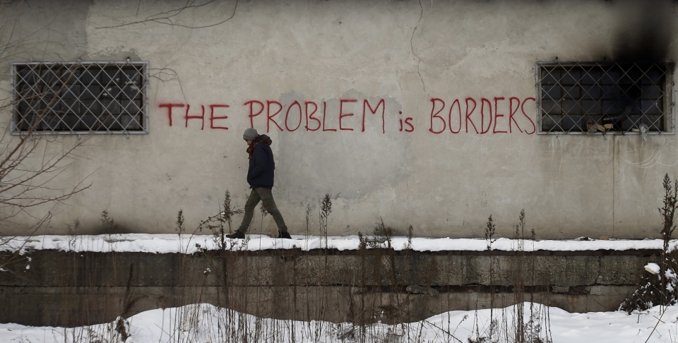 A migrant passes graffiti on a warehouse in Belgrade serving as a make-shift shelter for hundreds of men trying to reach Western Europe (AP Photo/Darko Vojinovic)
