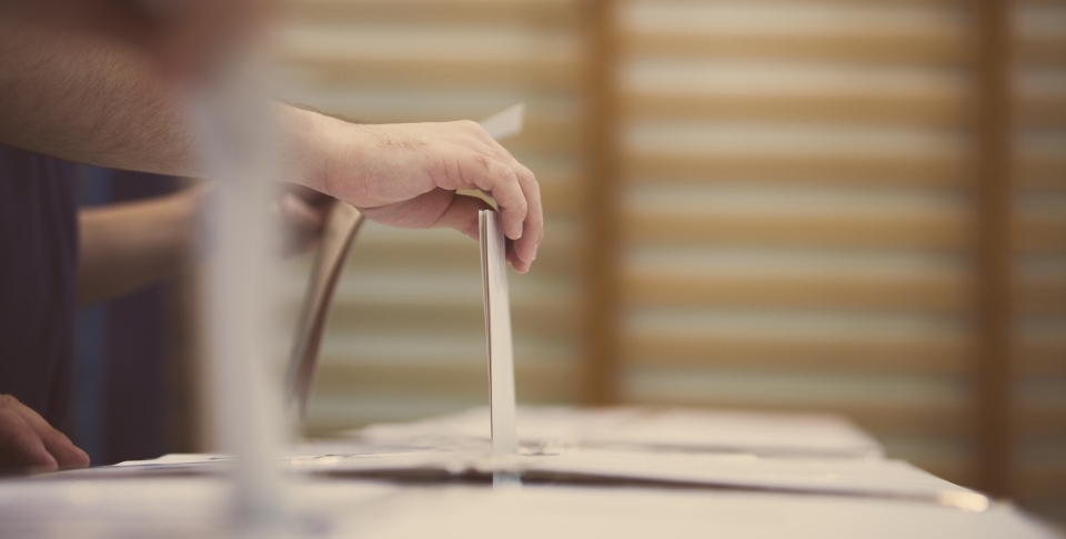 A voter slides a ballot into a ballot box (Shutterstock).