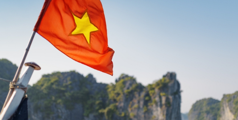 The flag of Vietnam (red flag with a gold star) fluttering on ship in the Halong Bay at the Gulf of Tonkin of the South China Sea, Vietnam. Karst towers-isles are visible in background/Shutterstock