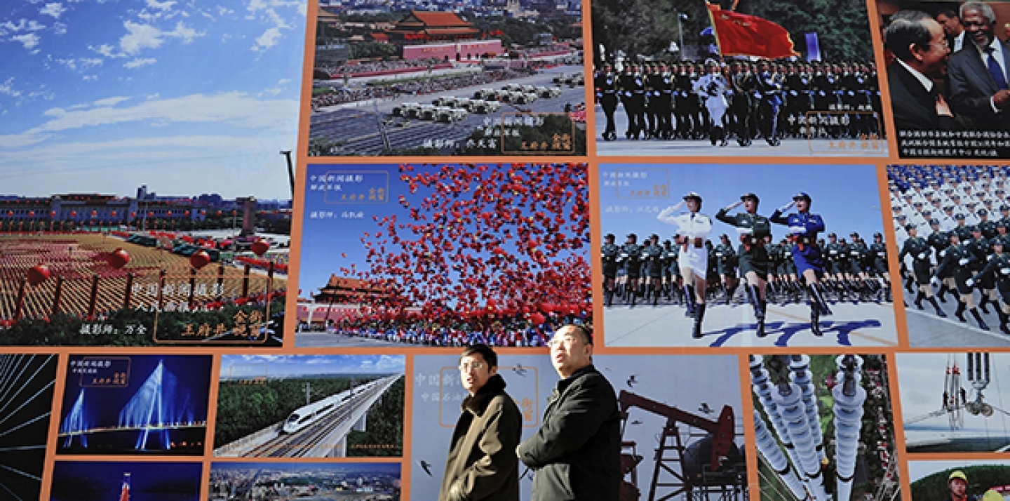 Two Chinese men walk past a huge billboard featuring photos of China's development in previous years in Beijing. (AP Photo/Andy Wong)