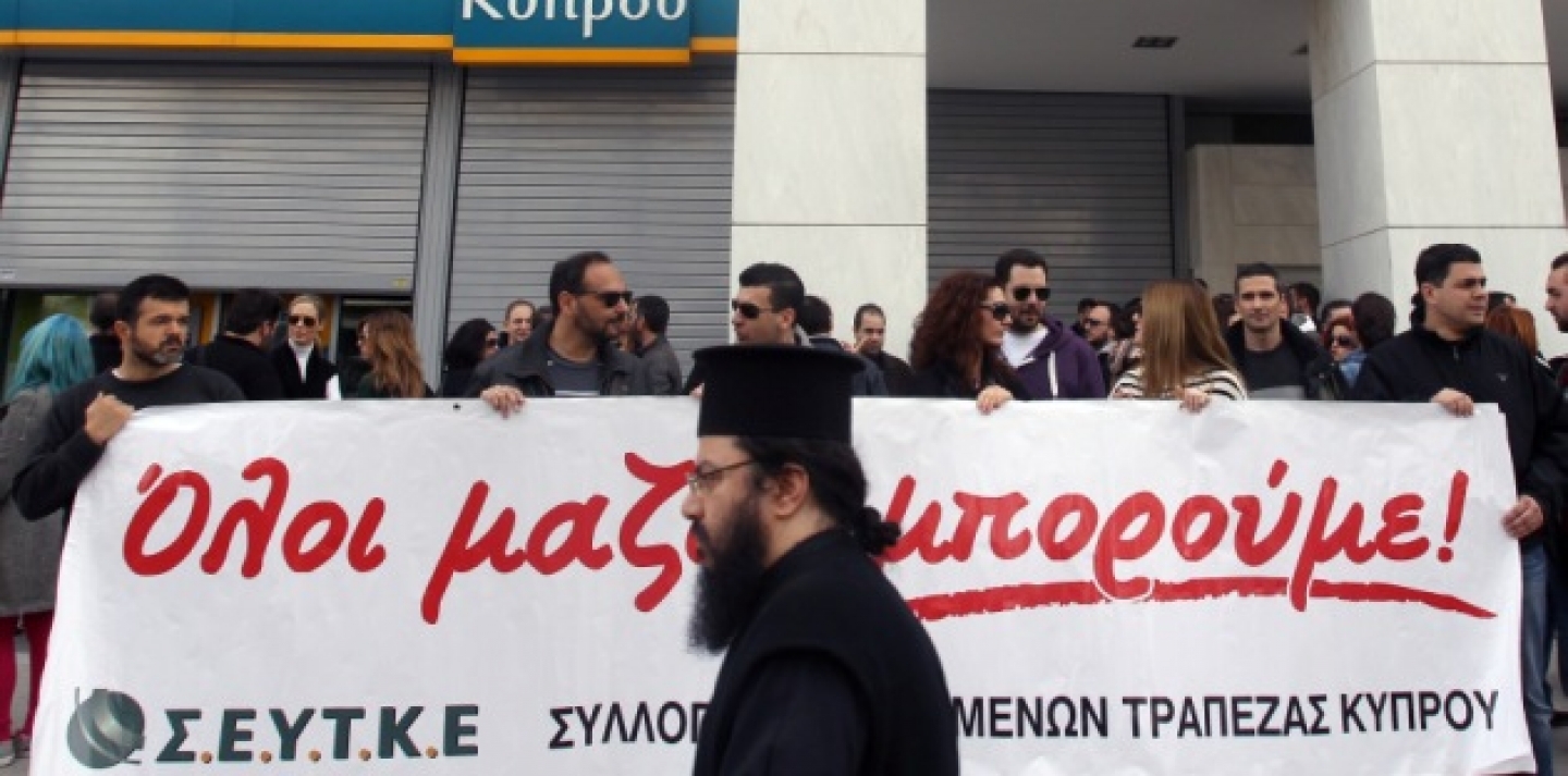 A Greek Orthodox priest passes employees of the Bank of Cyprus holding a banner that reads: ''All Together...We Can'' during a rally outside headquarters in Athens on Wednesday, March 20, 2013, following Cypriot lawmakers' rejection of a bailout plan. (AP Photo/Thanassis Stavrakis)
