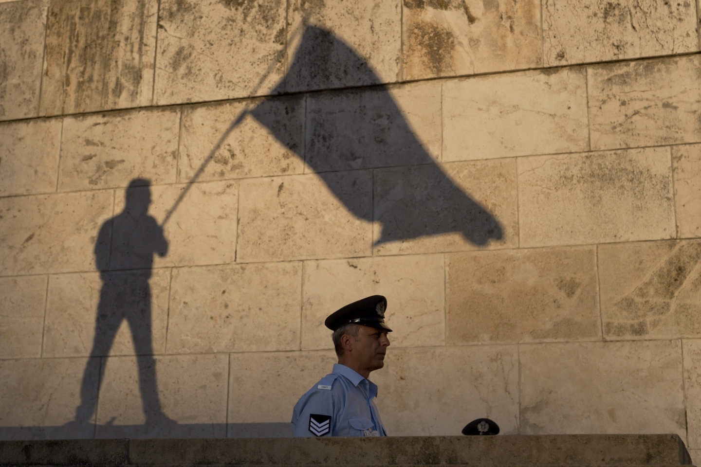 The shadow of a demonstrator waving a flag is cast on a wall as a Greek police officer secures the Greek Parliament during a protest in Athens (AP Photo/Petros Giannakouris)