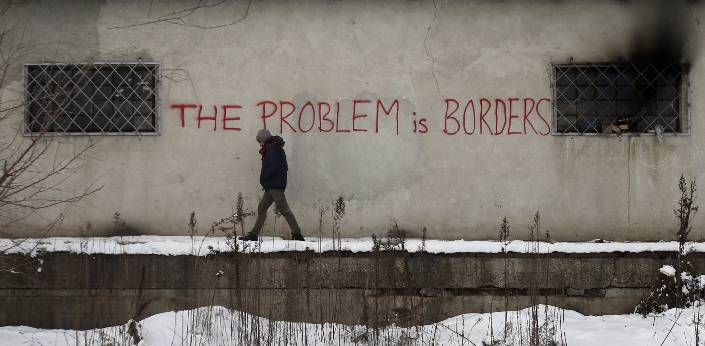 A migrant passes graffiti on a warehouse in Belgrade serving as a make-shift shelter for hundreds of men trying to reach Western Europe (AP Photo/Darko Vojinovic)