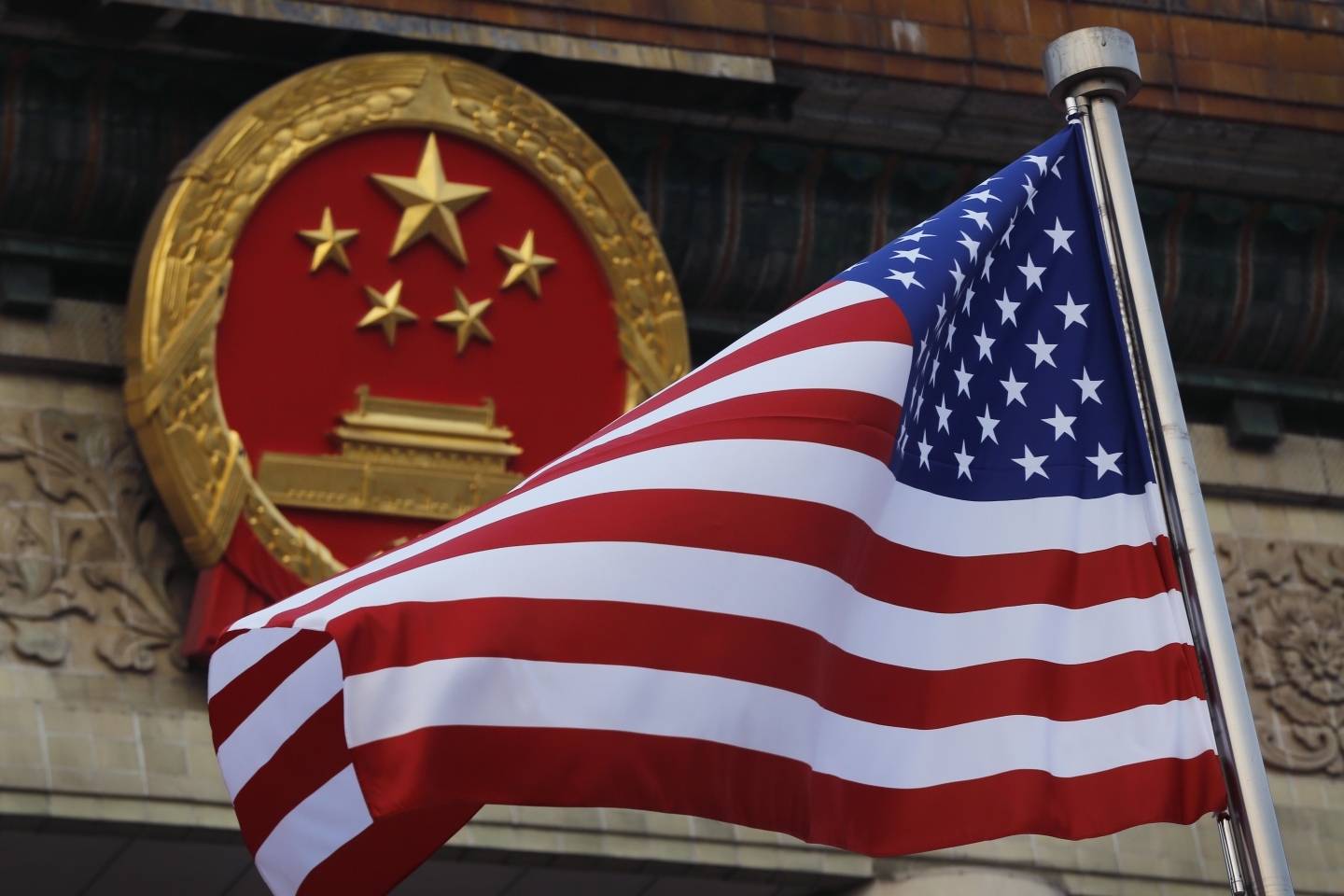 An American flag is flown next to the Chinese national emblem in Beijing (AP Photo/Andy Wong)