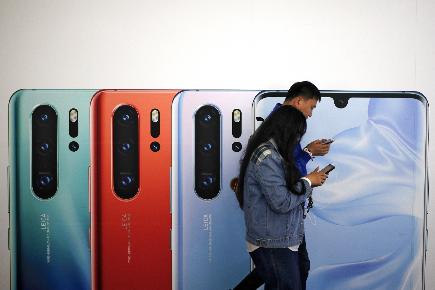 Two people browse their smartphones as they walk by a Huawei P30 smartphone advertisement in Beijing on May 13, 2019. (AP Photo/Andy Wong)