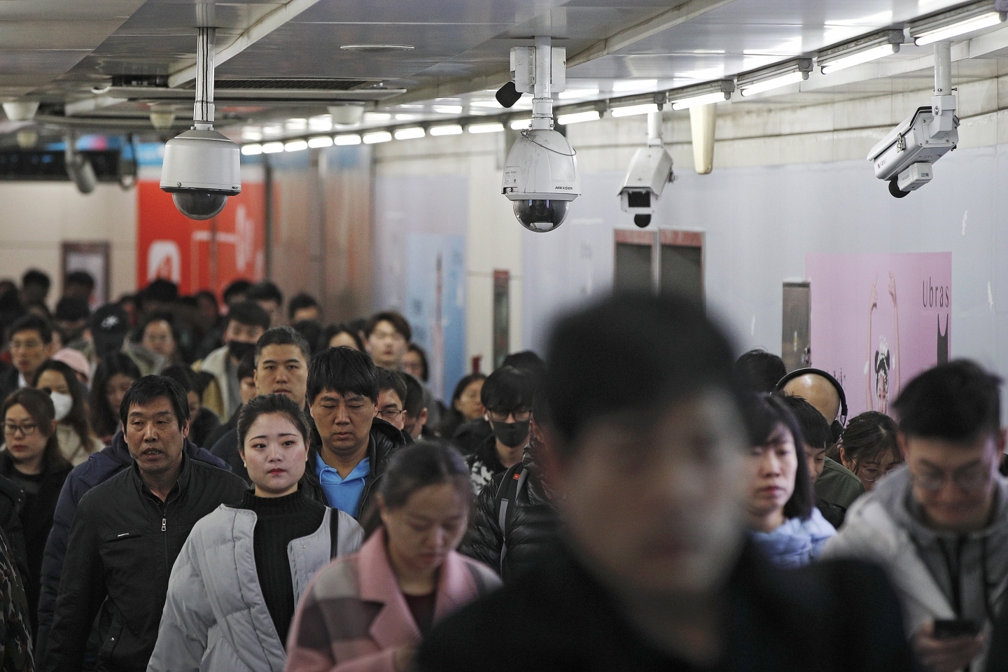 commuters walk by surveillance cameras installed at a walkway in between two subway stations in Beijing. (AP Photo/Andy Wong, File)