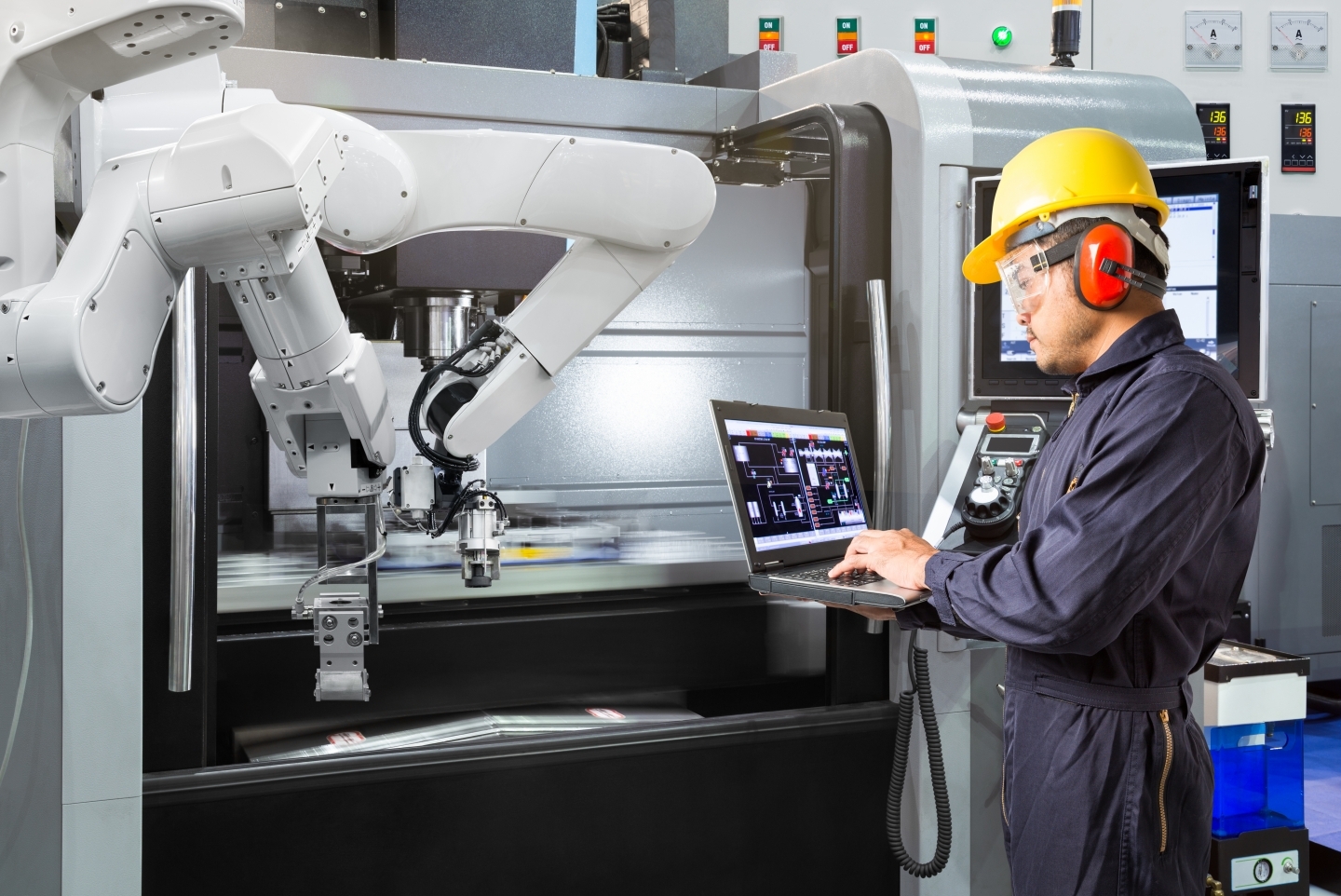 Maintenance engineer using laptop computer control automatic robotic hand with CNC machine in smart factory. (Shutterstock)
