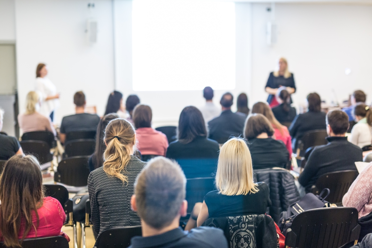 Two female university professors deliver a lecture to students in a classroom