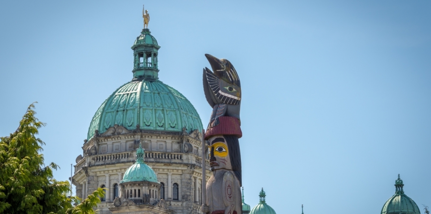 The Provincial Capital Legislative Parliament Building behind a First Nations totem pole in Victoria, British Columbia. (Shutterstock)