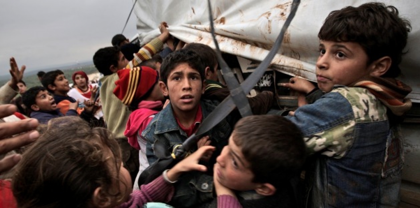 Syrian children who fled their homes gather around a vehicle to get pillows and blankets. This tent camp, sheltering some of the hundreds of thousands displaced, has lost the race against winter: the ground under their white tents is soaked in mud allowing rain water to seep into mattresses and bedding. (AP Photo/Muhammed Muheisen)