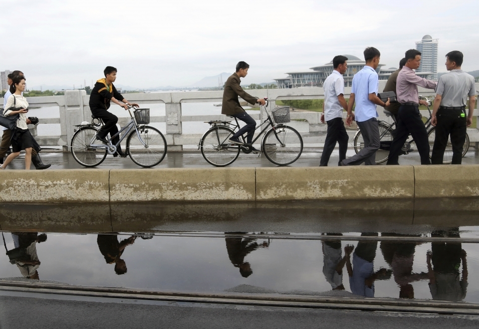 People are reflected in a puddle of water as they cross a bridge during the morning rush hour in Pyongyang, North Korea on June 15, 2018. (AP Photo/Dita Alangkara)