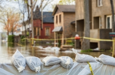 Sandbags with flooded homes in the background